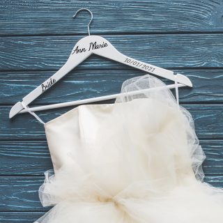 A white wedding dress hanging on a blue hanger with personalized vinyl label that reads a name and a date